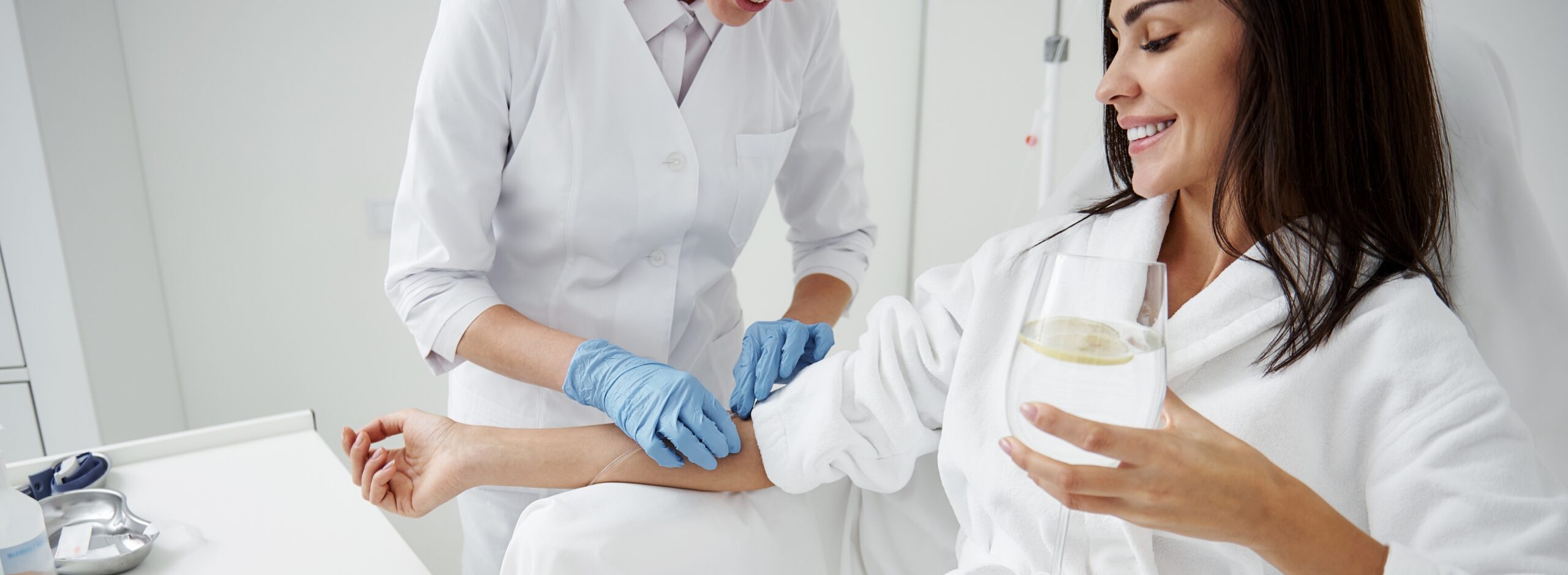woman holding a glass of lemon water receiving iv nutritional therapy