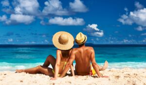 man and woman sitting together in the sand on the beach wearing sun hats