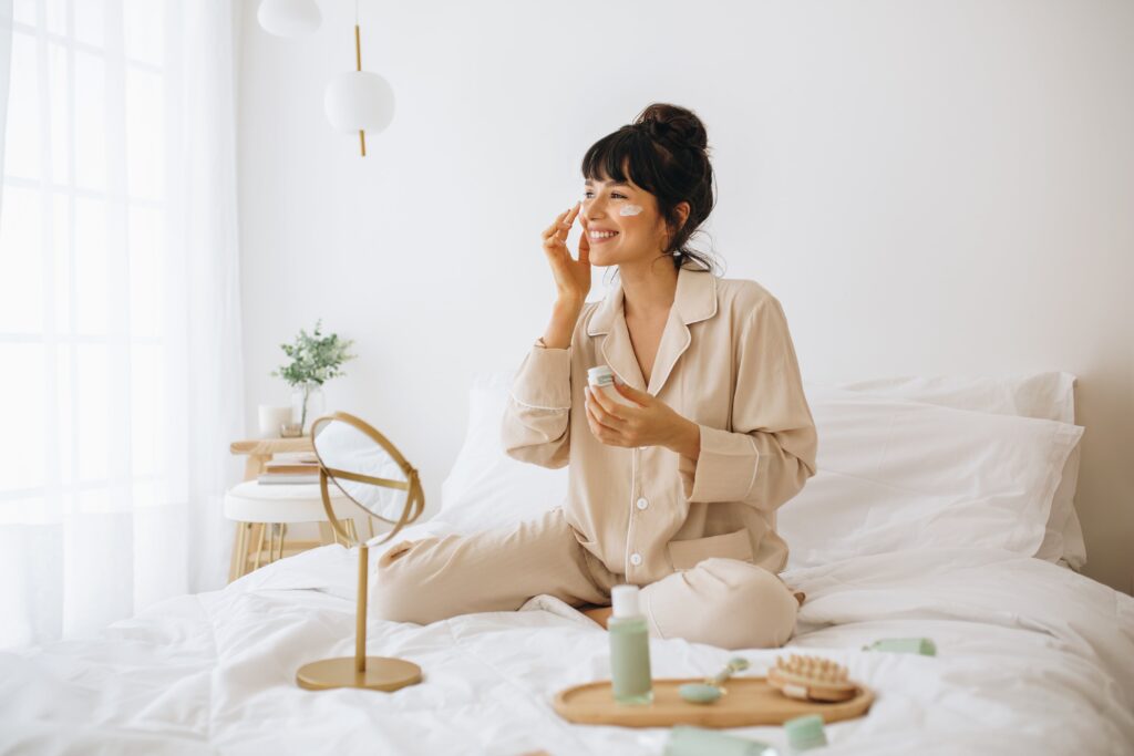 woman sitting in bed applying cream for winter skin care routine